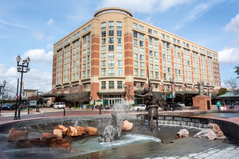 View of Sugar Land Town Square, with fountain, sculptures, building and city traffic. Sugar Land, Texas