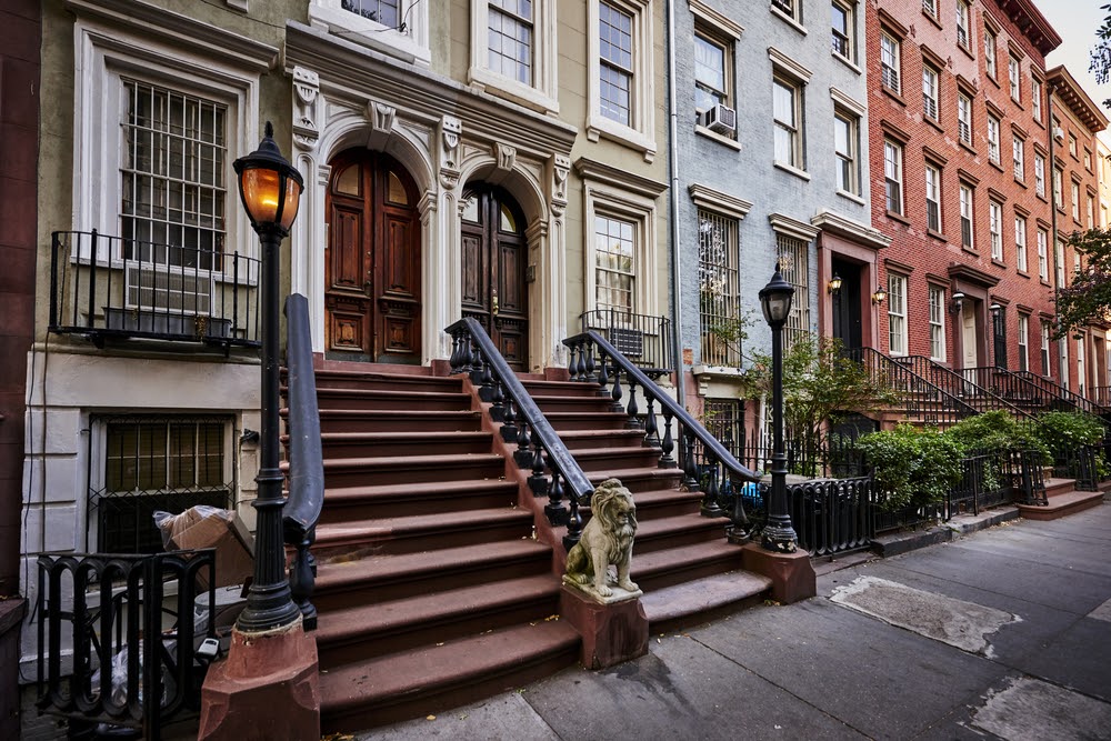 A row of colorful brownstone buildings with a warm gas lamp in a famous neighborhood in Manhattan, New York City.