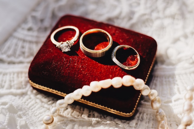 three rings and a pearls necklace on a red cushion