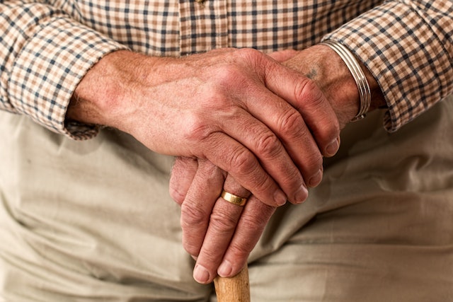 hands of an older man holding a walking stick 