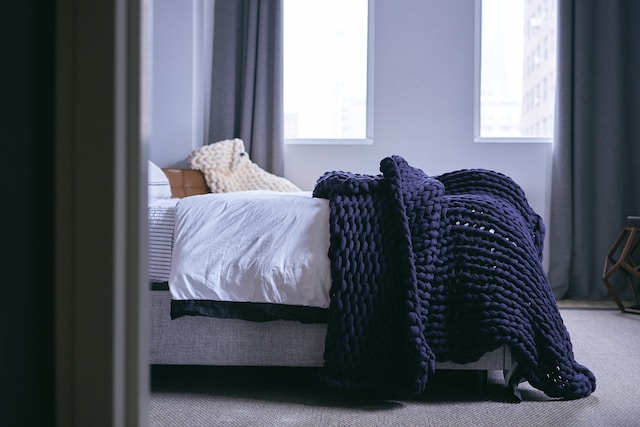 A side view of a bedroom with a mattress and a cozy knit blanket on top of it.